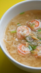 rice soup with shrimp in white bowl on yellow background