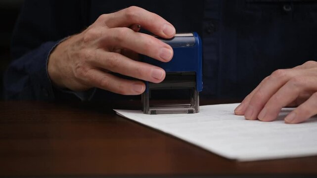 unknown businessman signs and stamps an official document. close-up of a male hands signing a contract, an agreement. concept of document management. front view.
