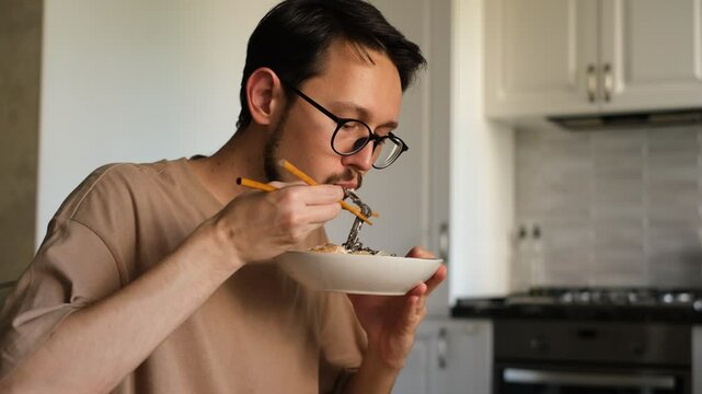 brunette man with a beard eats soba noodles with shrimp at home