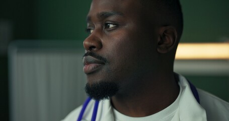 In a hospital setting, a young African physician poses with a warm smile, stethoscope draped around...