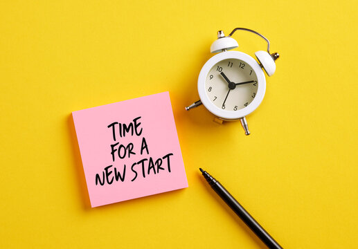 Time for a New Start message on pink note paper with alarm clock and pen. New beginnings in business career or life concept.