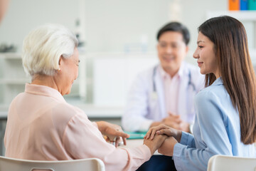 Fototapeta premium Asian male doctor give health advise to young woman and old woman at hospital kindness and warm. Young asian beautiful woman holds her mum hand give encouragement .
