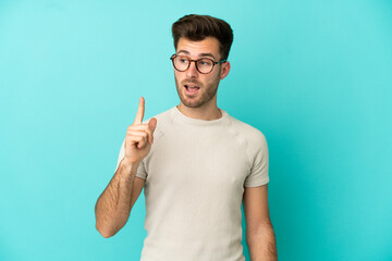 Young caucasian handsome man isolated on blue background intending to realizes the solution while lifting a finger up