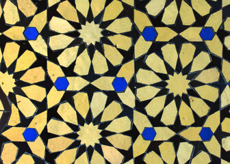 A detailed Islamic geometric mosaic featuring vibrant colors and symmetrical patterns. The design showcases traditional arabesque motifs with star shapes and interwoven lines