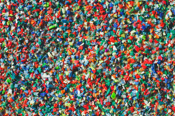 Multicolored recycled plastic granules in various shapes and sizes, creating a vibrant texture. The image represents sustainability, waste management, and environmental awareness