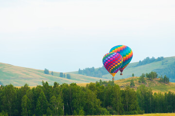 Obraz premium Colorful hot air balloons flying over the green hills and trees at sunset.