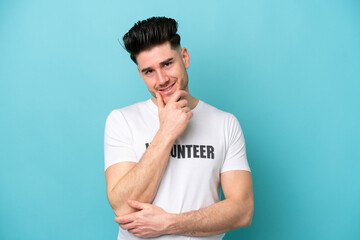 Young volunteer caucasian man isolated on blue background happy and smiling