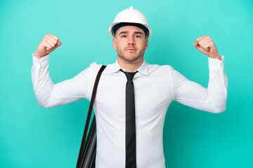 Young architect caucasian man with helmet and holding blueprints isolated on blue background doing...
