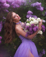 Portrait of a beautiful sensual woman in a lilac dress with a bouquet of flowers under a blooming lilac tree in a botanical garden.