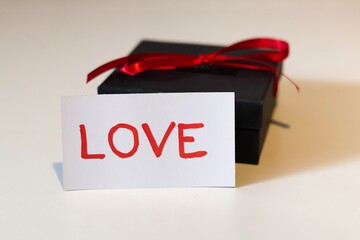 A black box with a red ribbon and a white card with the word 'love' written on it; An expression of love