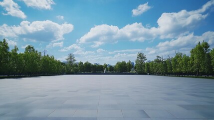 Open grey tiled square under a cloudy blue sky and surrounded by green trees