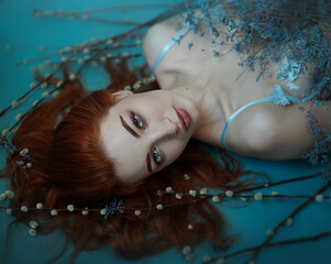 Close portrait of beautiful red-haired woman with blue eyes with flowers and pussy willow. View from above.