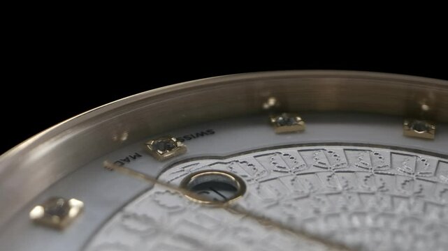 Upside down close-up view of rotating luxury swiss women's watch with white guilloche and shiny diamonds. Golden second arrow running by the watch face