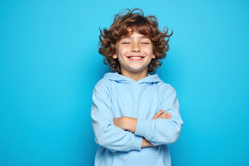 young boy with curly brown hair standing against blue background