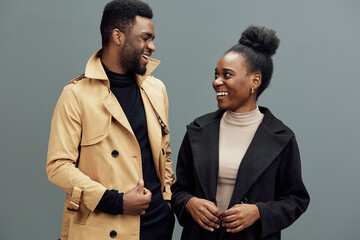 Happy couple dressed in stylish autumn outfits smiling against a grey background, showcasing modern fashion and joyful emotions in a cozy atmosphere