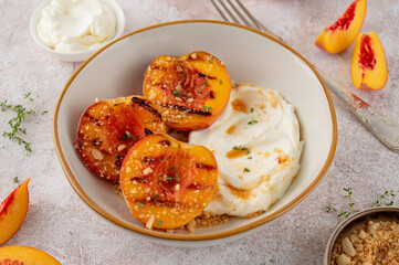 Delicious grilled peaches with mascarpone cream, honey syrup, crumbs and thyme in a bowl on a concrete background. Summer dessert. Top view.