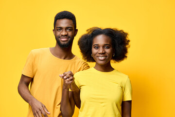 Obraz premium Happy young African couple in matching yellow outfits smiling together against a bright yellow background, symbolizing joy, love, and togetherness
