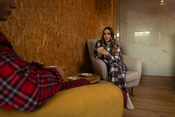 Obraz premium Relaxed young couple sitting in comfortable armchairs, drinking steaming coffee and sharing intimate conversation during lazy weekend morning at home