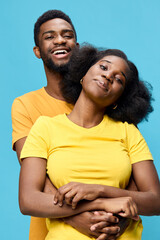 Obraz premium Young African couple in bright yellow and orange t shirts, smiling happily against a vibrant blue background A joyful representation of love and connection