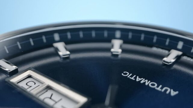 Closeup view of rotating luxury swiss watch with metallic second arrow passing by on blue clock face with beautiful guilloche on blue background