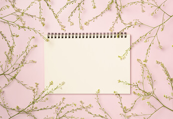 Empty notebook with frame of flowers on pink background. Flat lay, top view. Space for text