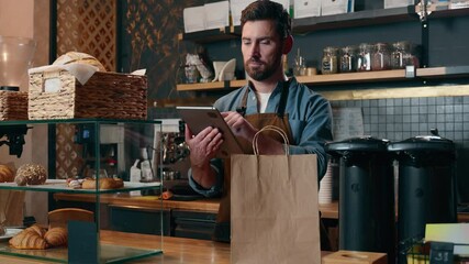 Smiling Caucasian guy delivery barista man calculate order price bill on tablet tech small business in cafeteria store catering restaurant waiter worker male give package food for client cafe service