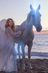 Young long-haired woman in a white dress riding a white horse against a seascape