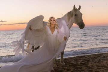 Young long-haired woman in a white dress riding a white horse against a seascape