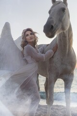 Young long-haired woman in a white dress riding a white horse against a seascape