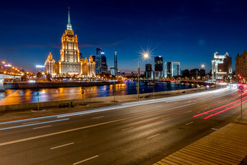 Illuminated high-rise stalinist building near river at summer night in Moscow, Russia. Historic name is Hotel Ukraina. Translation of the inscription on the facade: Ukraine