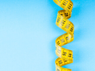 Close-up of a coiled yellow measuring tape on a light blue background, ideal for health, fitness,...