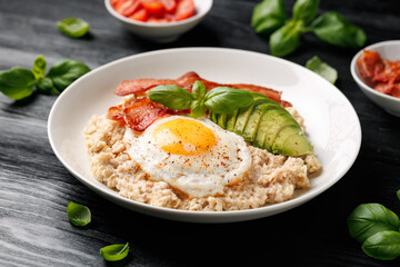 Savory Oatmeal breakfast with sunny side up fried egg, bacon and avocado. Healthy food
