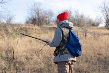 Mature hunter man holding a shotgun and walking through a field