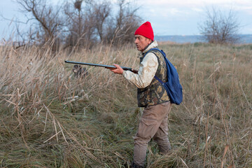 Mature hunter man holding a shotgun and walking through a field