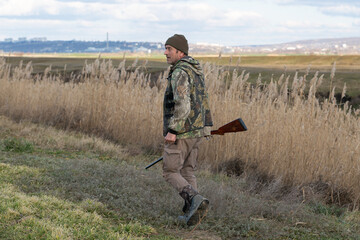Mature hunter man holding a shotgun and walking through a field