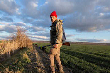 Mature hunter man holding a shotgun and walking through a field