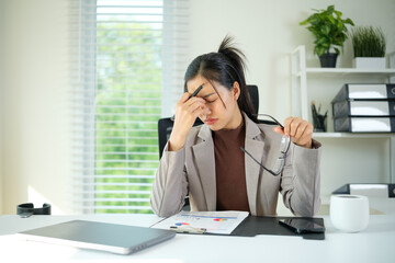 Tired businesswoman holding her head while removing her glasses, conveying workplace stress or decision fatigue.