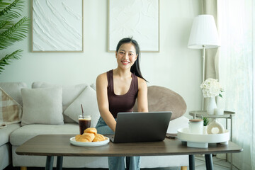 A woman enjoying her work-from-home setup with a laptop and refreshments in a well-decorated living room.