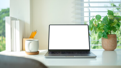 Fototapeta premium White desk with a laptop, coffee mug, green potted plant and books.