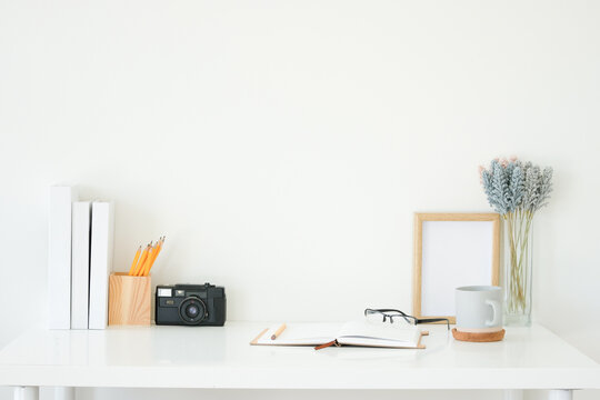 Creative workspace with glasses, coffee cup, notebook and photo frame on white desk.