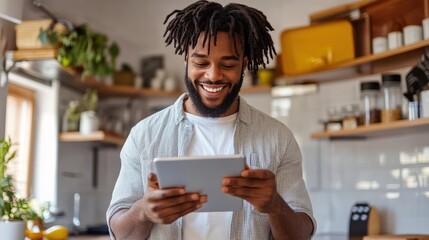 Fototapeta premium Black man using a tablet while cooking in a cozy kitchen. Natural light and fresh ingredients create a warm atmosphere, blending digital convenience with a modern culinary lifestyle.