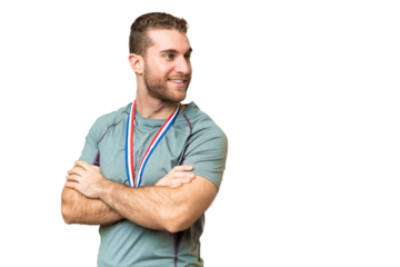 Young handsome blonde man with medals over isolated chroma key background with arms crossed and happy