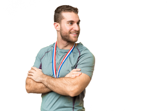 Young handsome blonde man with medals over isolated chroma key background with arms crossed and happy
