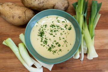 Top view of Vichyssoise soup, potatoes and leek on a wooden cutting board.