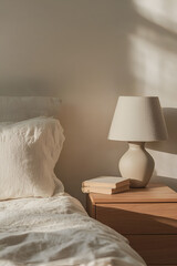 A minimalist bedroom scene with soft linens, a bedside lamp, and a stack of books on a wooden nightstand.