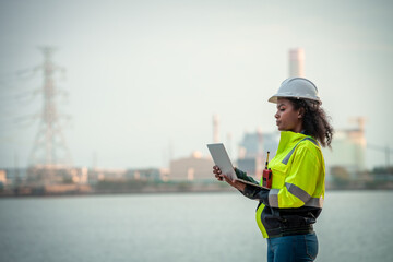Engineers wearing safety gear, including hard hats examining survey standing industrial facility...