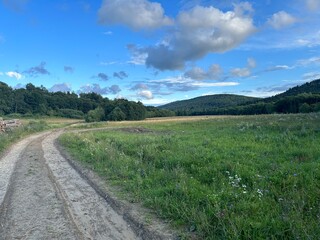 Rural Dirt Road Through Green Fields and Hills Under Blue Sky