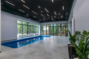 Indoor swimming pool with high-tech interior decoration. Panoramic windows with a view of the summer landscape.