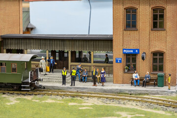 train station platform with passengers waiting, railway staff assisting, and a vintage green train ready for boarding