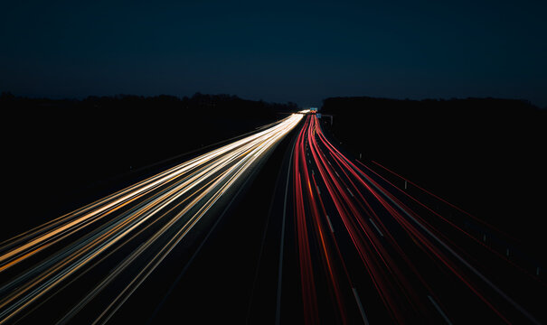 A long-exposure photograph capturing highway traffic at night, creating stunning light trails. The image shows bright white and red streaks from vehicle headlights and taillights against a dark backgr